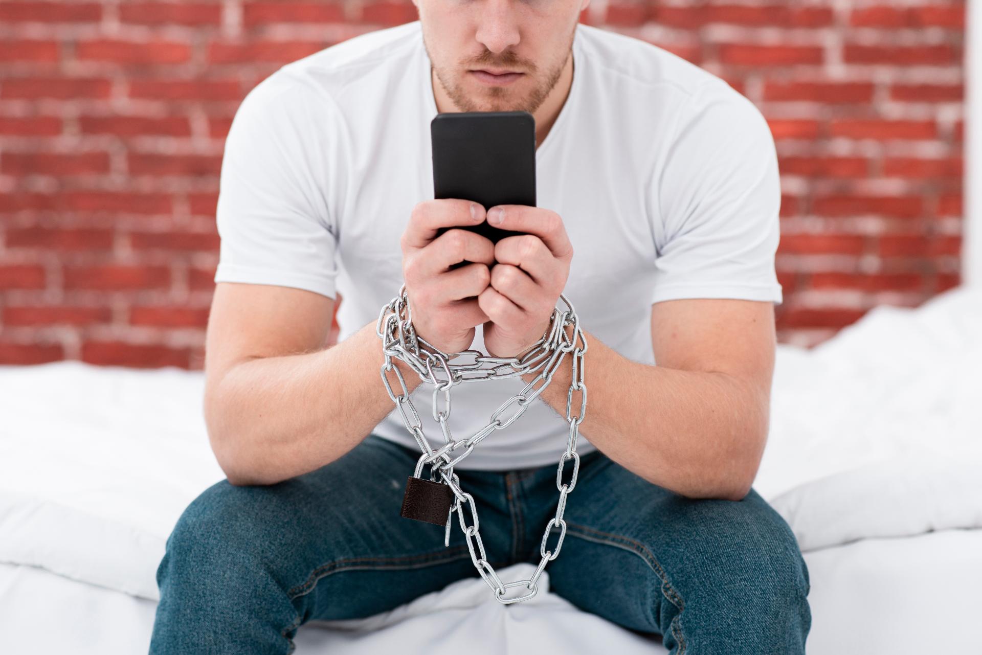 Man Holding His Phone While He Is Tied Up With Chains